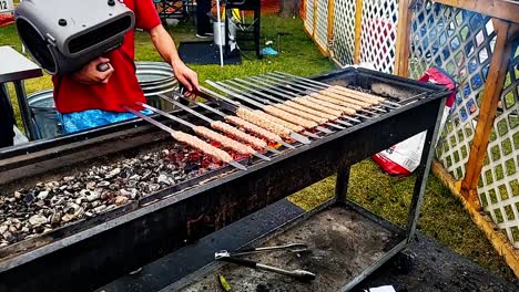 closeup bbq skewers of meat rotating with electric blower over charcoal grill with person adjusting the meat before they sell them