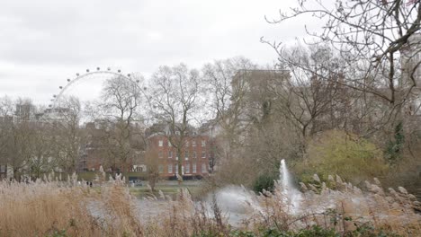 a calm park scene with a fountain, trees, and the london eye visible in the distance