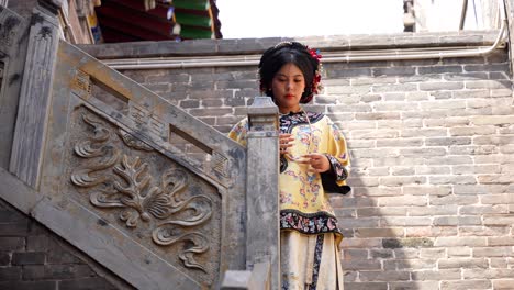 Toma-De-ángulo-Bajo-De-Una-Mujer-Con-El-Vestido-Tradicional-Qing-Posando-En-Las-Escaleras-Y-Hablando-En-Pingyao,-China.