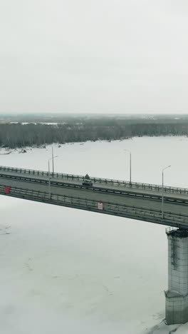 flycam films tremendous bridge with pylons running over white frozen river for fast moving vehicles bird eye view
