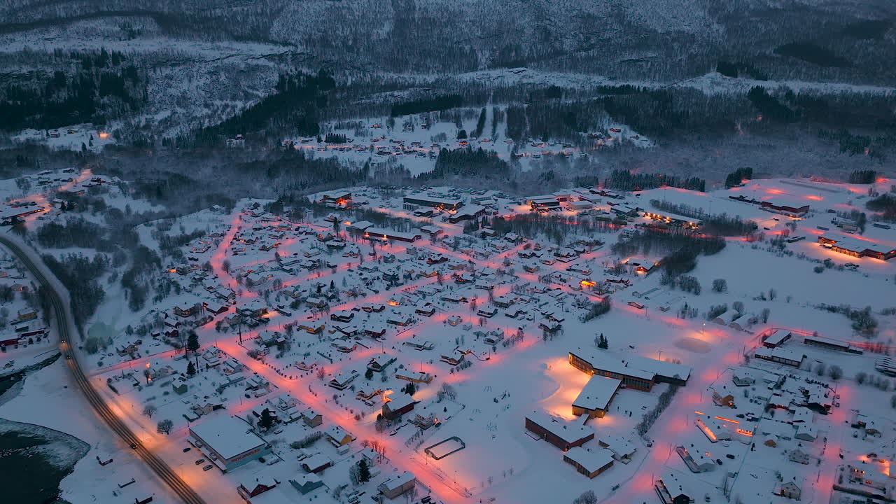 Korkealta otettu dronen kuva pienestä norjalaisesta kaupungista, joka on lumen peitossa ja jonka lämpimät katuvalot hehkuvat sinisen hetken aikana. Ihanteellinen matkailu-, talvikausi- ja arktisen elämäntavan sisältöön.