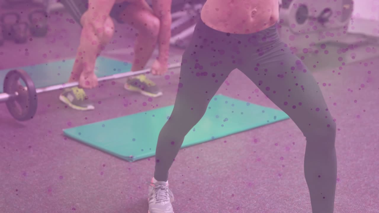 Woman holding dumbbells on mat while man initiating barbell clean, powering paired fitness strength