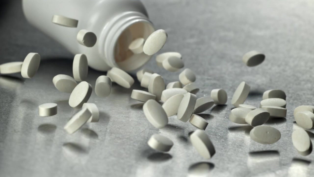 Movimento rallentato di pillole bianche che cadono da un flacone di medicinali
