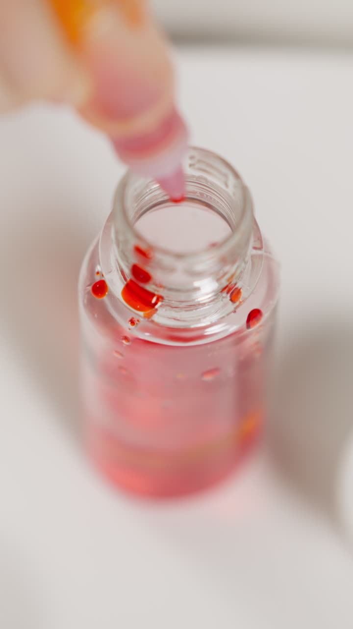 Little girl drips red paint into glass bottle from plastic tube with pipette during performing chemical experiment in laboratory extreme upper close view
