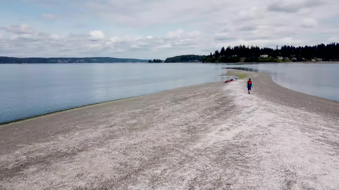 low aerial shot traveling along an island sandbar past a walking man