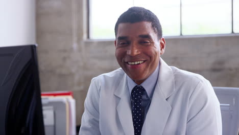 smiling mixed race doctor in lab coat sitting in the office