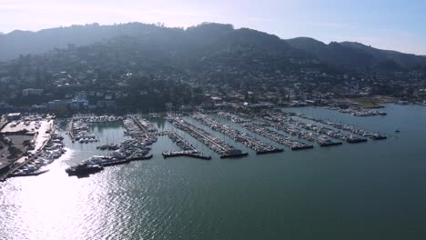 Vista-Desde-Un-Dron-Sobre-El-Bullicioso-Puerto-Deportivo-De-Sausalito,-Yates-Amarrados-En-Ordenadas-Filas,-Rodeados-De-Verdes-Colinas,-Con-Un-Toque-De-San-Francisco-A-Lo-Lejos.