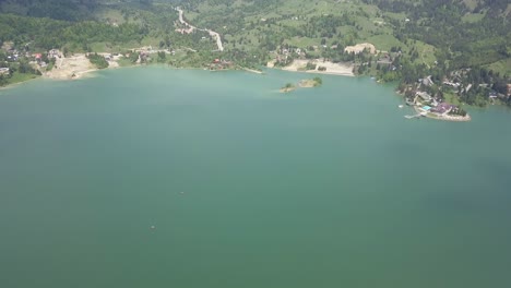 Toma-Panorámica-Descendente-Aérea-Del-Lago-Con-Bosques-Verdes-En-Un-Día-Soleado