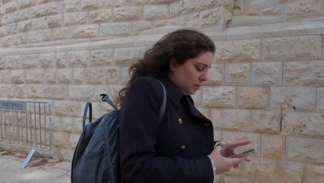 woman walking and looking at smartphone near a stone wall