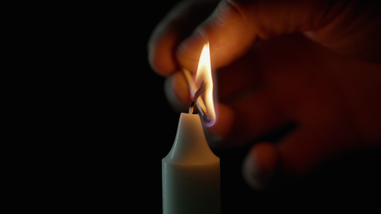 Gros plan d’une personne allumant une bougie à la paraffine avec une allumette en bois sur fond noir