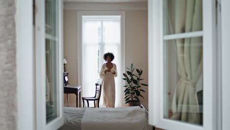 domestic girl open curtains at morning indoors. african woman enjoying espresso