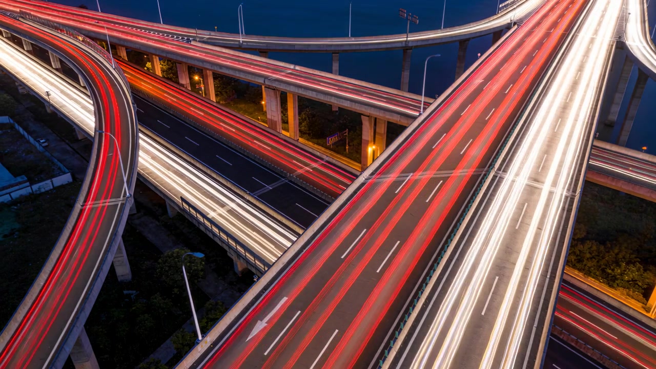 Mostrando uno svincolo autostradale a più livelli che crea scie luminose rosse e bianche dal flusso del traffico.
