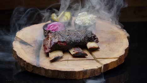 perfectly grilled hot bbq ribs on a rustic wooden plate with pickles and a cloud of a smoke medium tilt-up shot