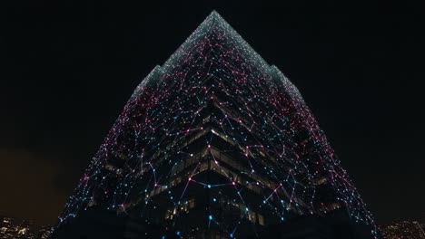 a stunning night view of a modern building illuminated with colorful led lights, showcasing a unique geometric design against the dark sky, capturing a fusion of architecture and technology
