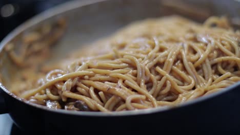 mixing nutritious spaghetti with sauce and mushroom in a hot skillet - close up