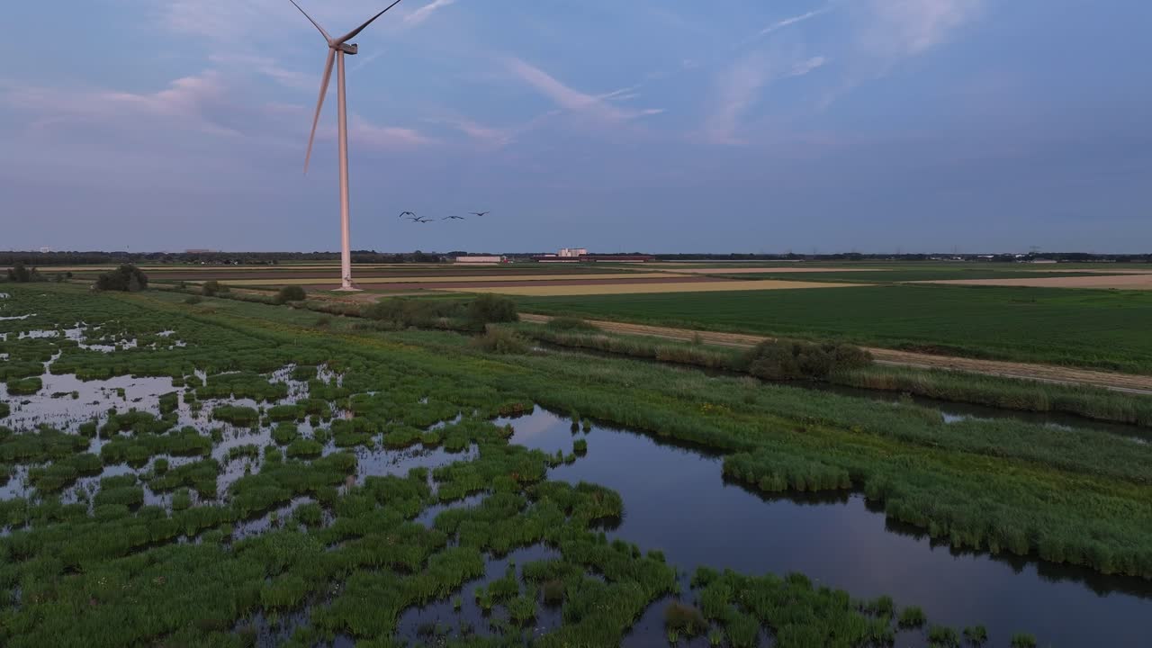 풍력 터빈은 황혼에 울창한 녹색 습지를 내려다보고, 평온한 물 채널을 반영합니다.