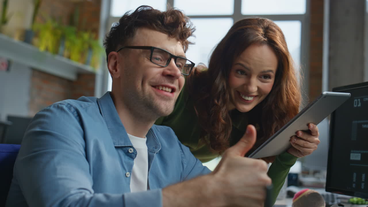 Two coworkers laughing video calling by computer in creative agency closeup