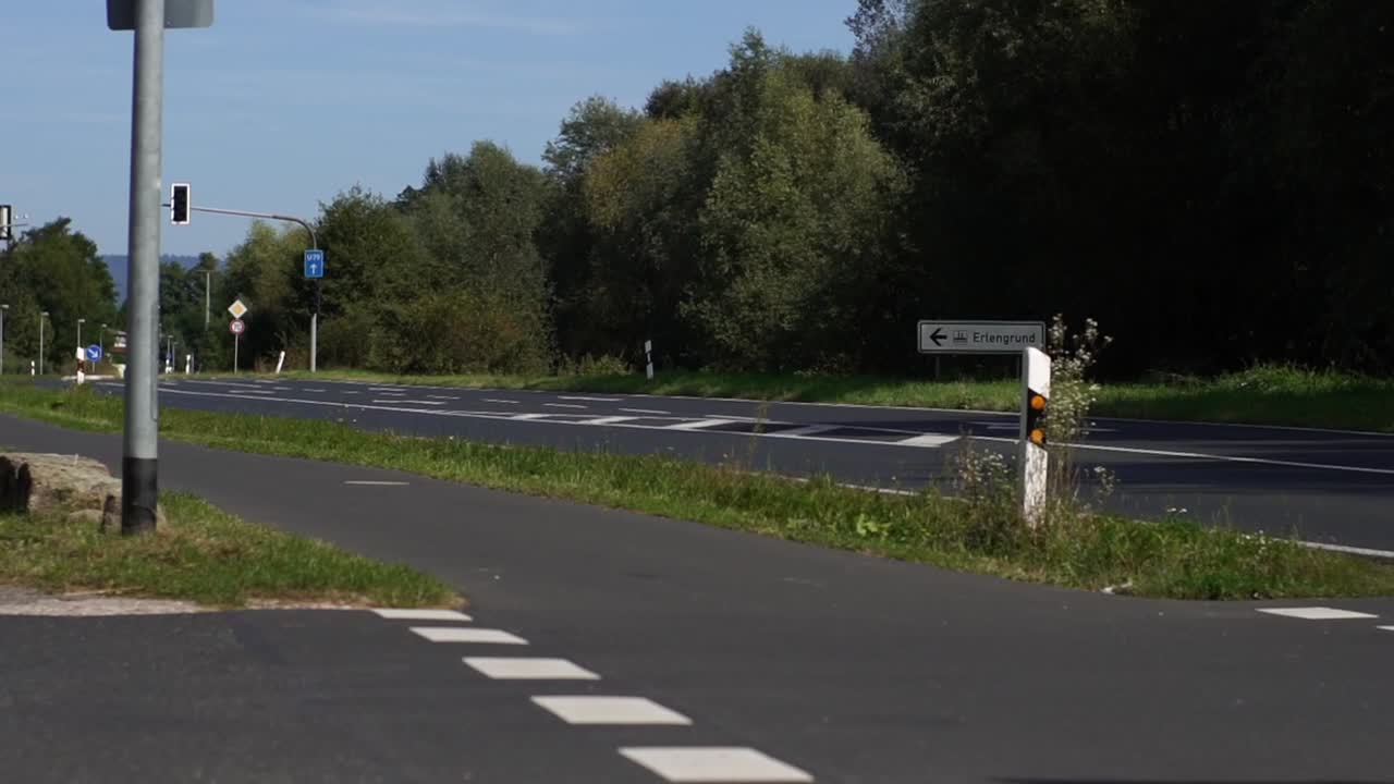 A sunlit road in Germany with car traffic passing through a forest, blending natural beauty with modern transportation. Ideal for nature, travel, and environmental projects showcasing scenic routes.