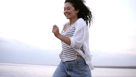 young, happy, cheerful brunette girl happily running by seaside in casual clothes. freedom, healthy lifestyle