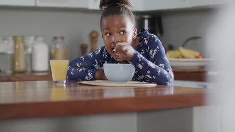 african american girl sitting at countertop and eating breakfast in kitchen, slow motion