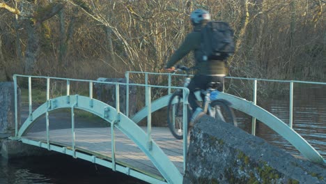 cyclist crossing walk bridge along forest trail over river