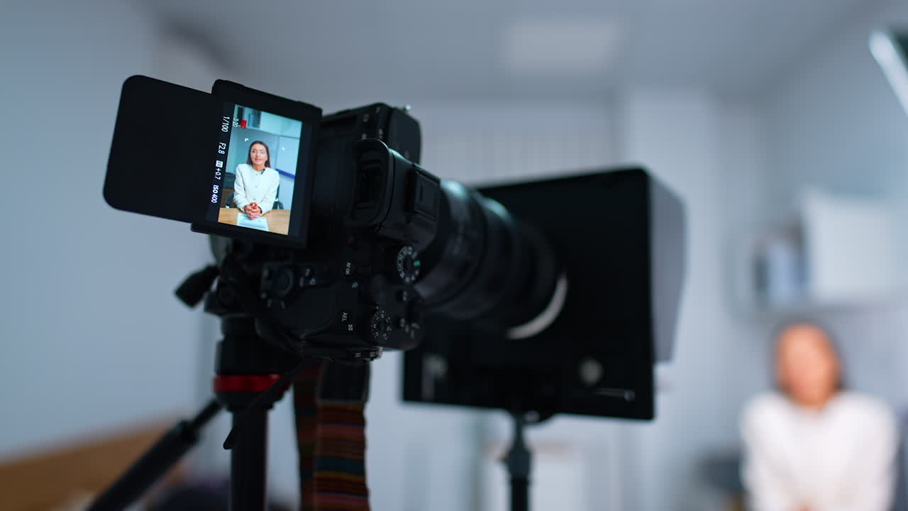 Camera on tripod with a display showing a Caucasian woman. Close up. Blurred backdrop. Blogging concept.