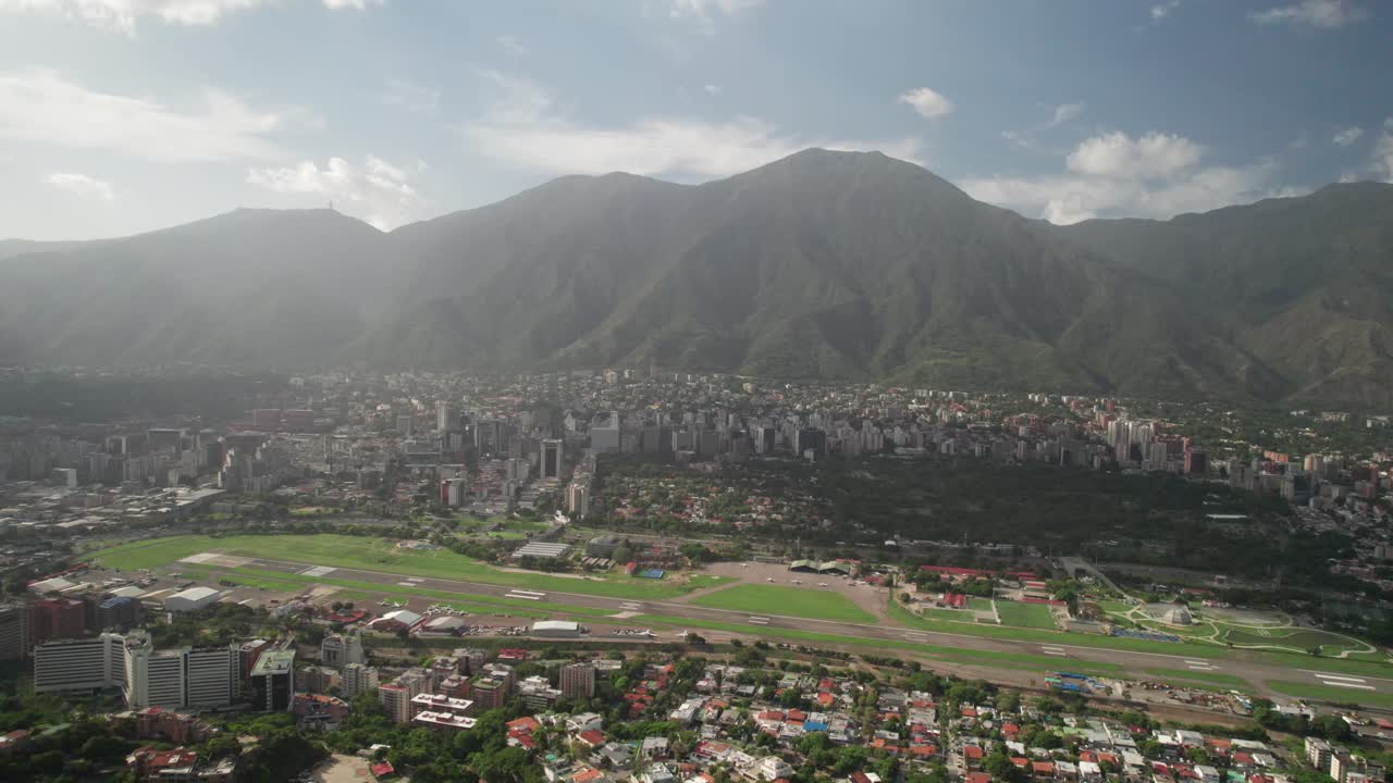 Drone tilts up from Santa Sofía revealing La Carlota cityscape in Caracas, Venezuela