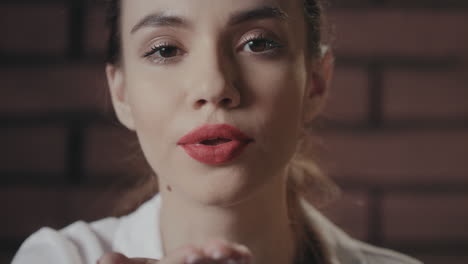 sexy woman with red lips sending kiss from hand to camera on brick background