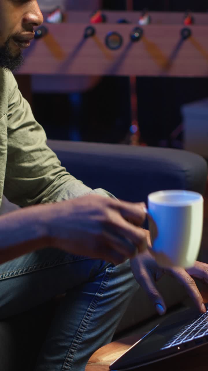 Vertical Video African American young adult working remotely on a laptop under loft neon lights