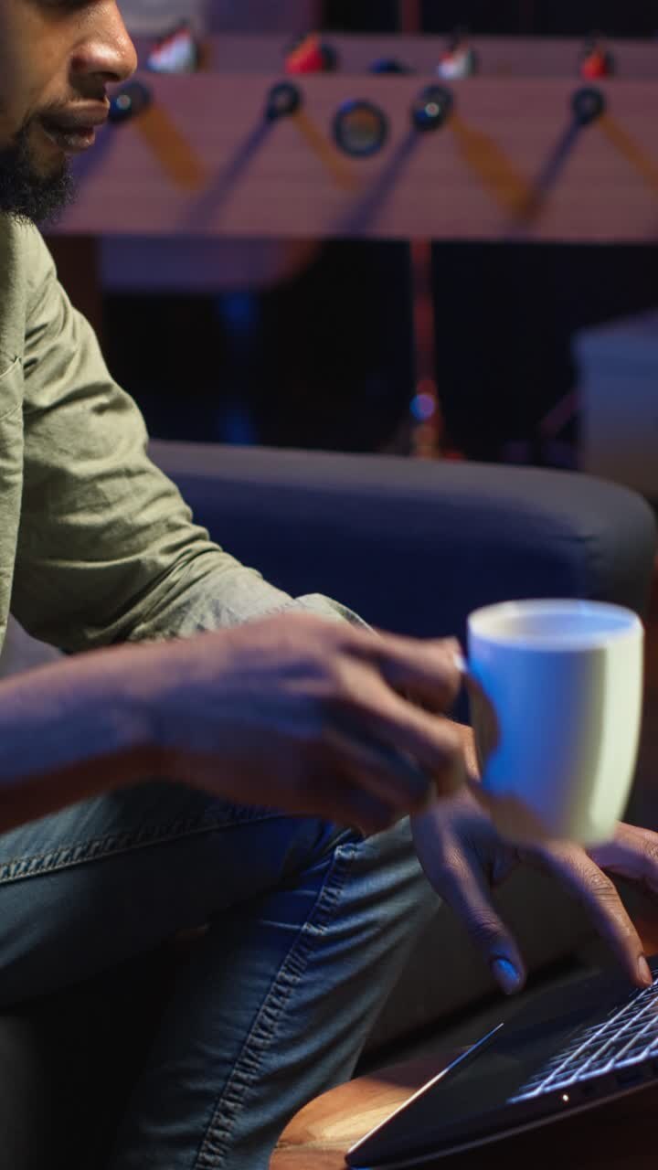 Vertical Video African American young adult working remotely on a laptop under loft neon lights