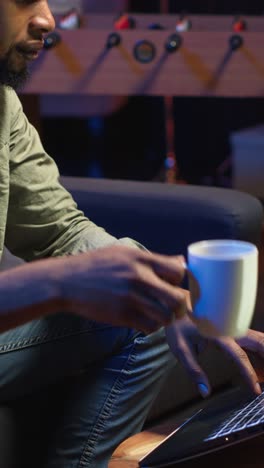 vertical video african american young adult working remotely on a laptop under loft neon lights