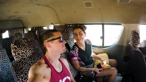 una pareja sonriendo y besándose en un minibus con asientos de impresión de leopardo, con destino a la playa