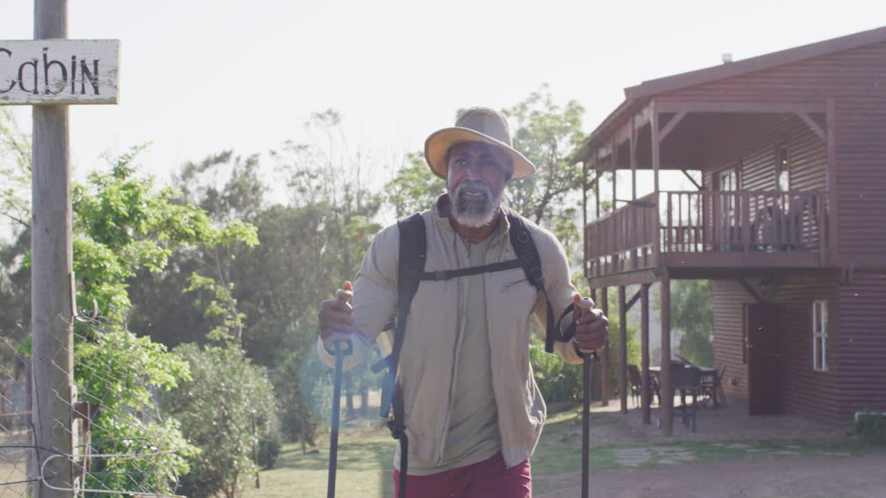 Senior african american man hiking with trekking poles on sunny day, slow motion