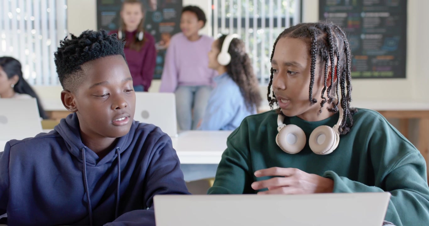 Diverse youth students two male students leaning asking typing on laptop working task trio smiling