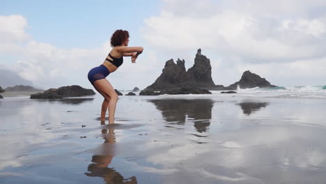 una mujer joven y delgada practica estiramiento y yoga en la orilla del océano, su mirada dirigida a la distancia en cámara lenta