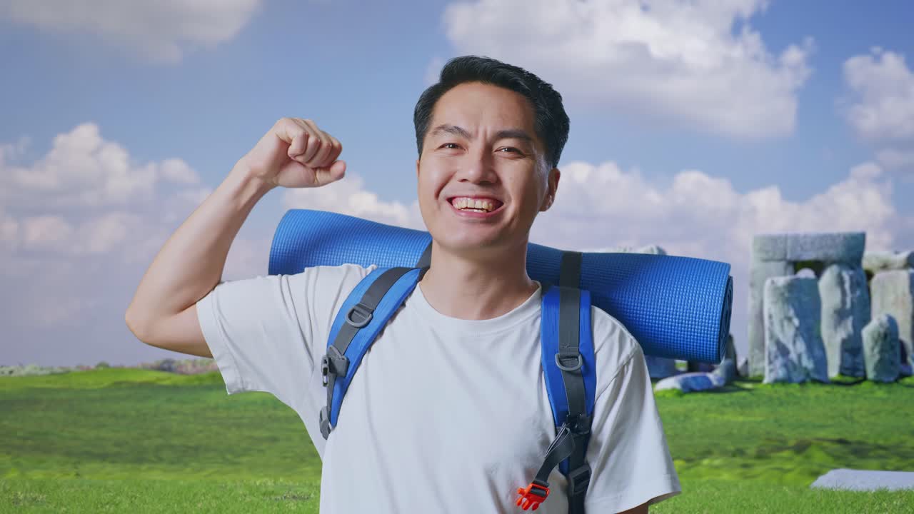 Close Up Of Asian Male Hiker With Mountaineering Backpack Smiling And Flexing His Bicep While Traveling In Stonehenge