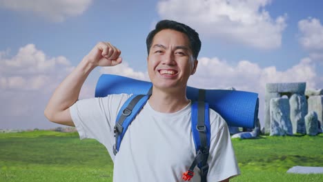 close up of asian male hiker with mountaineering backpack smiling and flexing his bicep while traveling in stonehenge