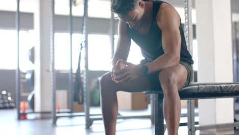 resting on bench, muscular man in gym wearing tank top and shorts
