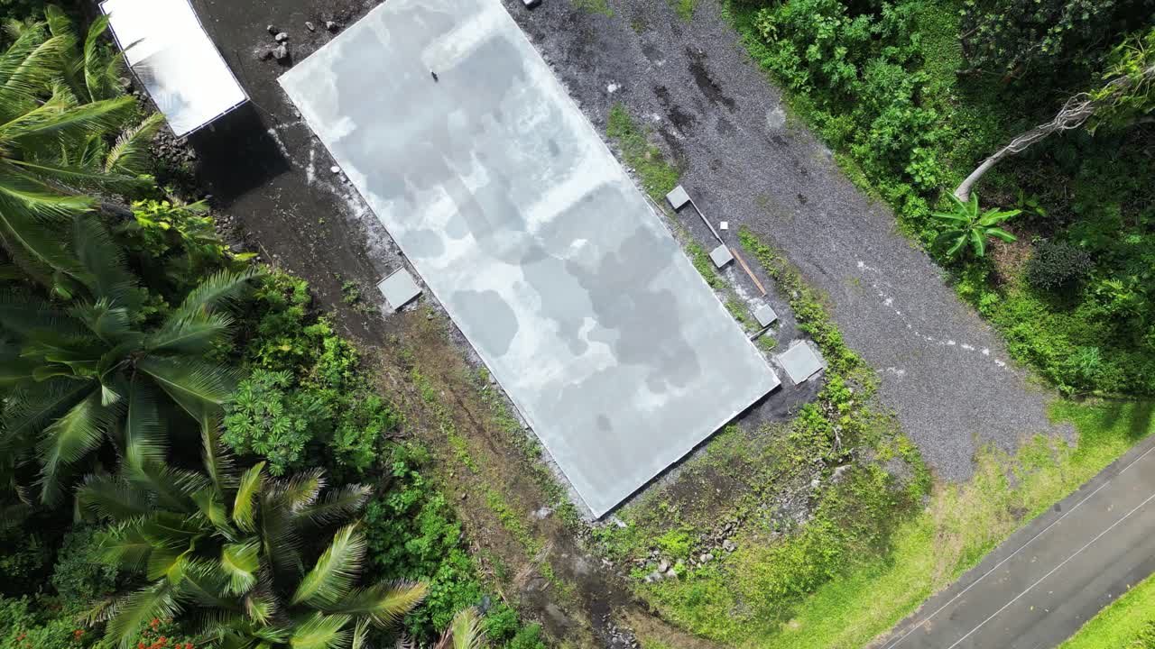 Aerial top-down pullback of concrete house foundation surrounded by tropical trees on Big Island, Hawaii.