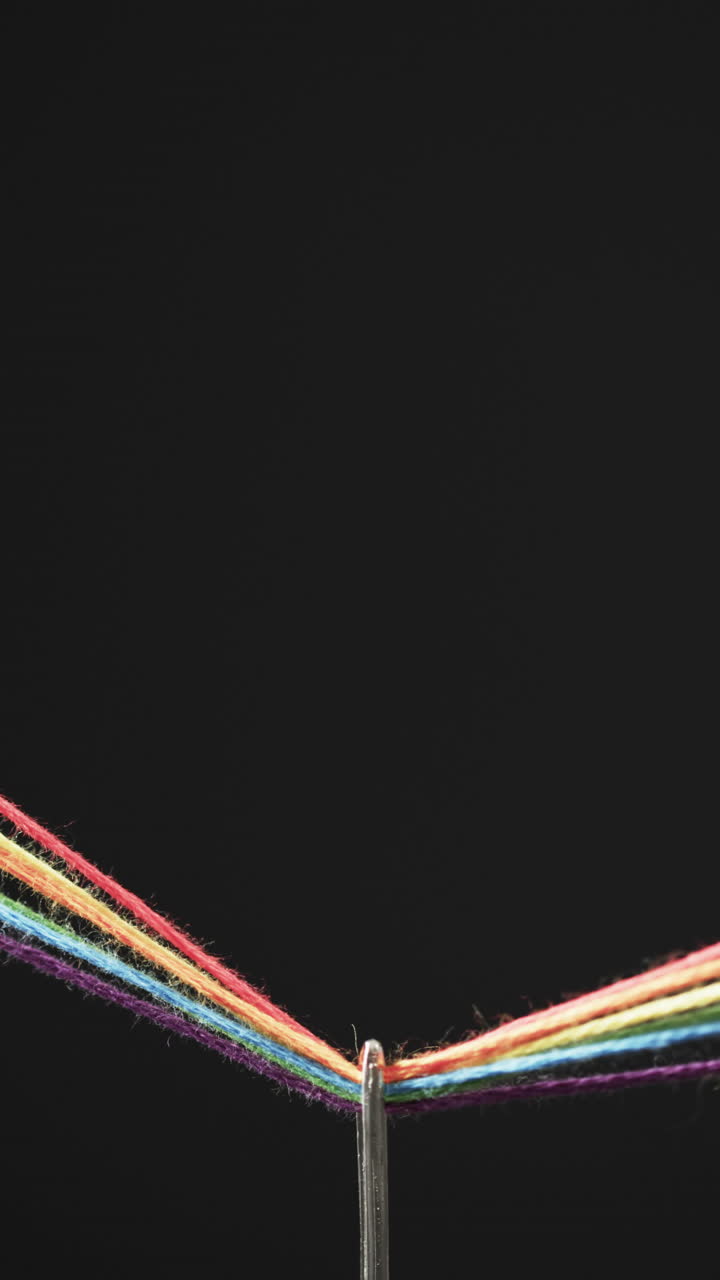 Vertical video of micro of needle with rainbow coloured threads and copy space on black background