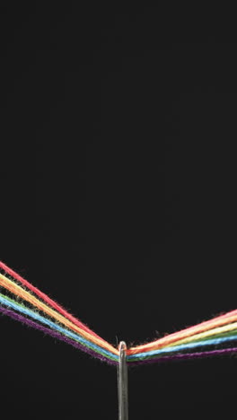 vertical video of micro of needle with rainbow coloured threads and copy space on black background