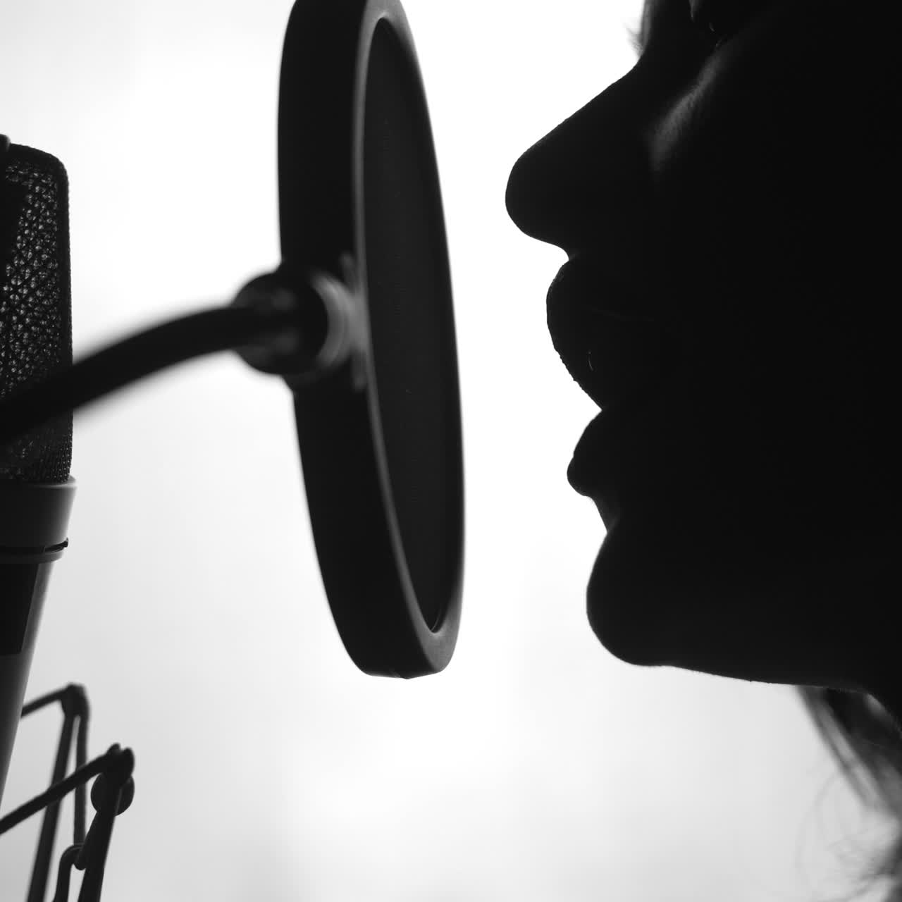 Professional singer in front of a microphone performing a song in studio. Attractive profile view of a female face singing. Close-up. Black and white video