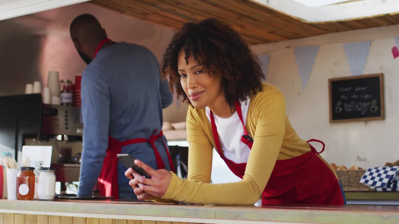 Portrait of smiling african american woman wearing apron using smartphone standing in the food truck