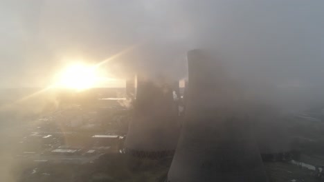 Aerial-view-of-power-station-cooling-towers-revealed-through-smoke-steam-emissions-at-sunrise