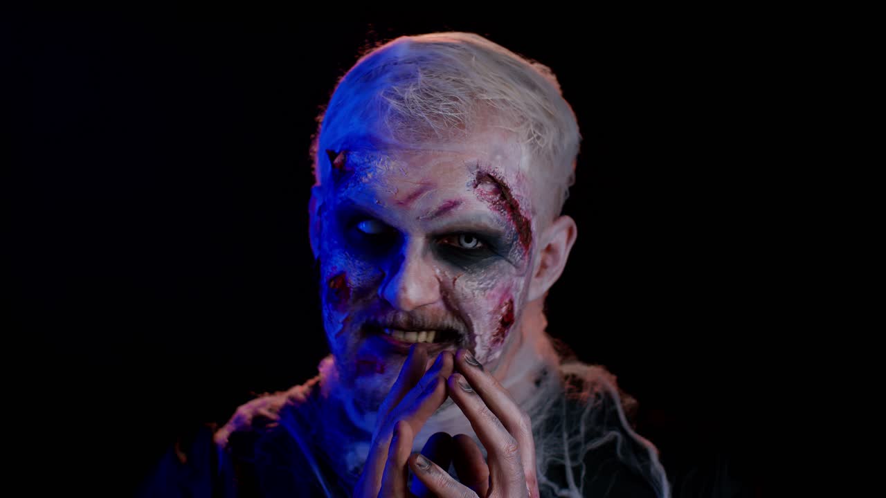 hombre muerto viviente herido aterrador con cicatrices sangrientas cara haciendo caras, mira a la cámara y sonríe terriblemente