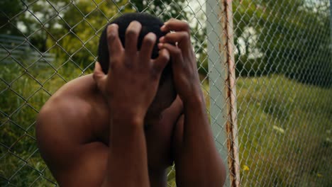 un hombre con el torso desnudo y la piel negra está molesto porque perdió un partido de baloncesto. un hombre tiene las manos sobre la cabeza como una señal de su fracaso, está molesto y cansado