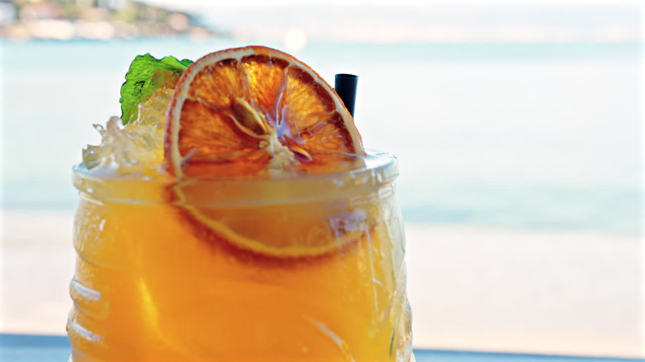 Close up of an orange cocktail on a table with a blurred view of the sea on the background