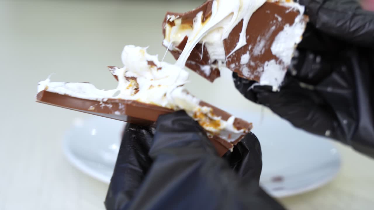 Close-up of gloved fingers holding gooey chocolate with marshmallow—perfect for food content, desserts, and ads.