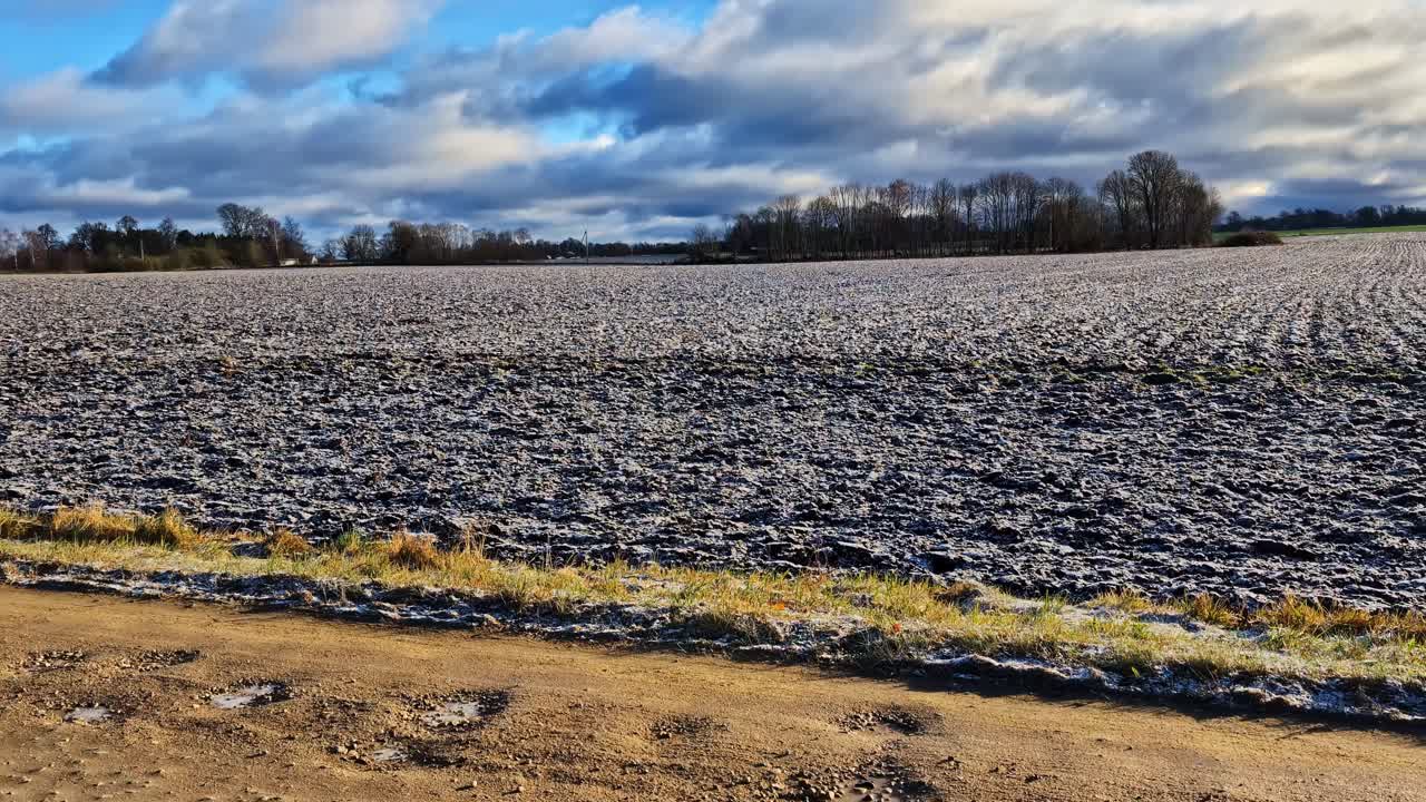 Expansive agricultural field covered in frost beneath a cloudy sky during winter