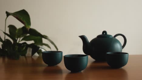 Fondo-Mínimo-De-Un-Juego-De-Té-Japonés-Verde-Con-Vapor-Saliendo-De-Las-Tazas,-Sobre-Una-Mesa-De-Madera,-Con-Una-Planta-En-La-Parte-De-Atrás